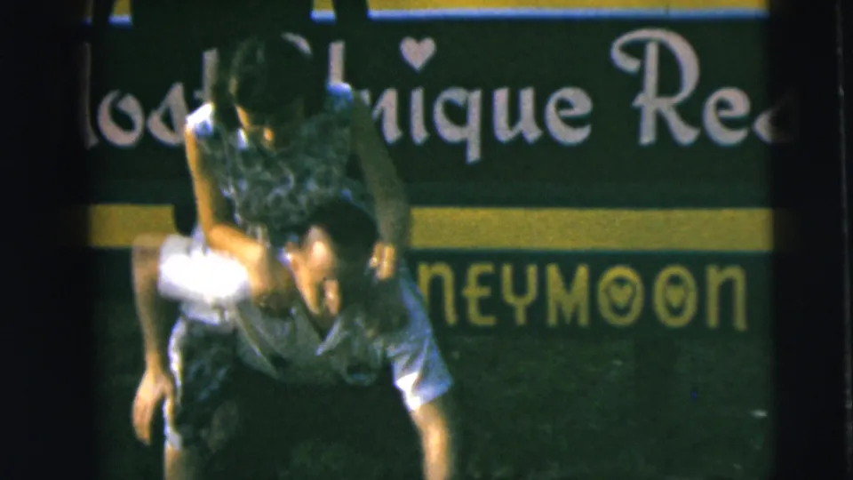 In the final frame, the woman is on the man's back while he bends forward in front of the Camden sign and grass.