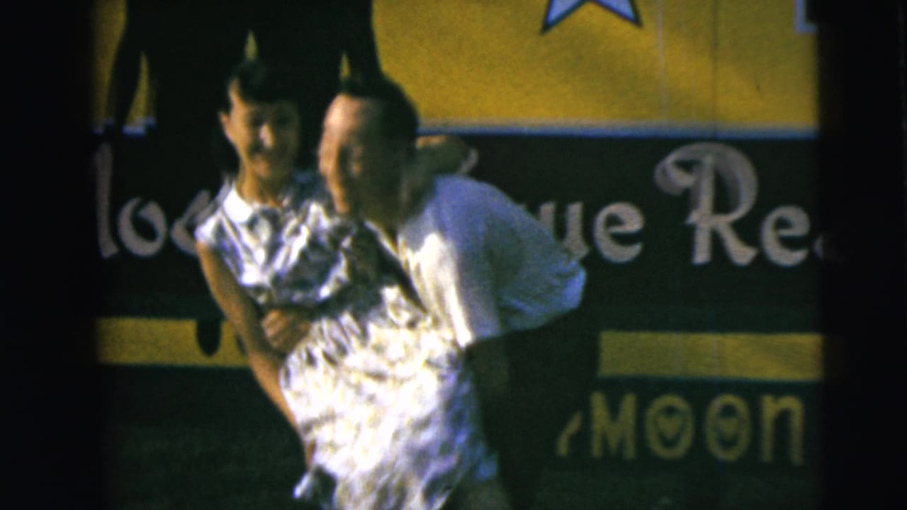 1962 Camden frame showing a smiling couple close together during a dance or playful pose before partial honeymoon-themed signage.