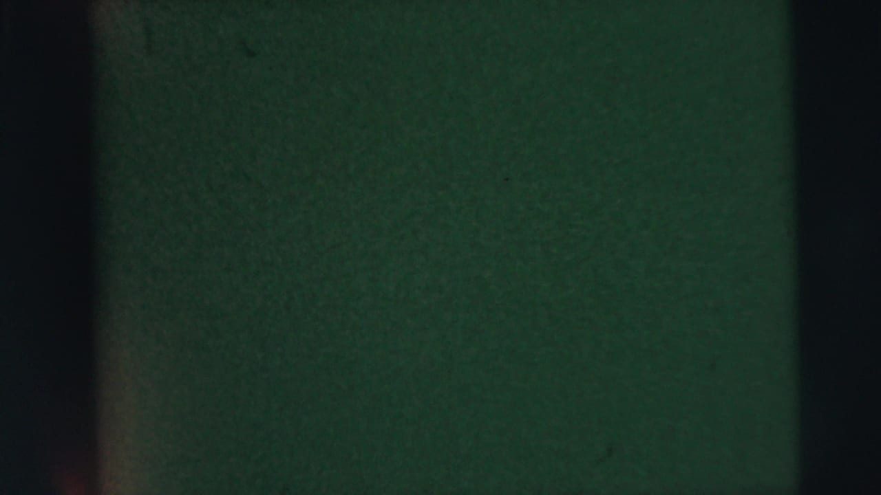 Dark exposed 8mm frame with green-black cast, vertical gate bands, and visible film grain from the 1962 Camden home-movie clip.