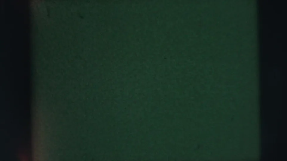 Dark exposed 8mm frame with green-black cast, vertical gate bands, and visible film grain from the 1962 Camden home-movie clip.
