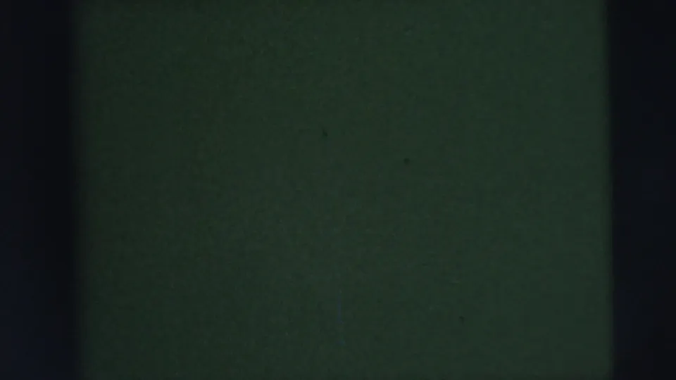 Underexposed 8mm frame showing vertical gate edges, green-black static, and faint reddish color near the left border.