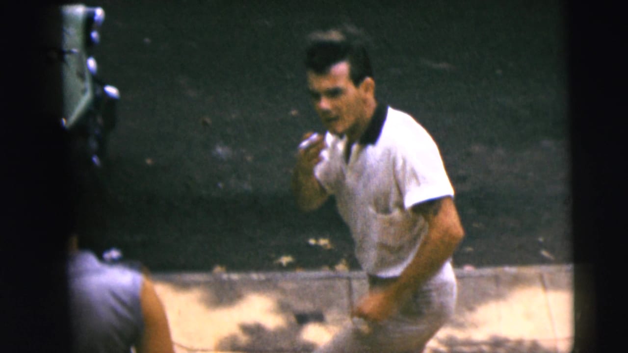 In 1962 Camden home-movie footage, a man in a white polo shirt smokes while standing near a street edge.