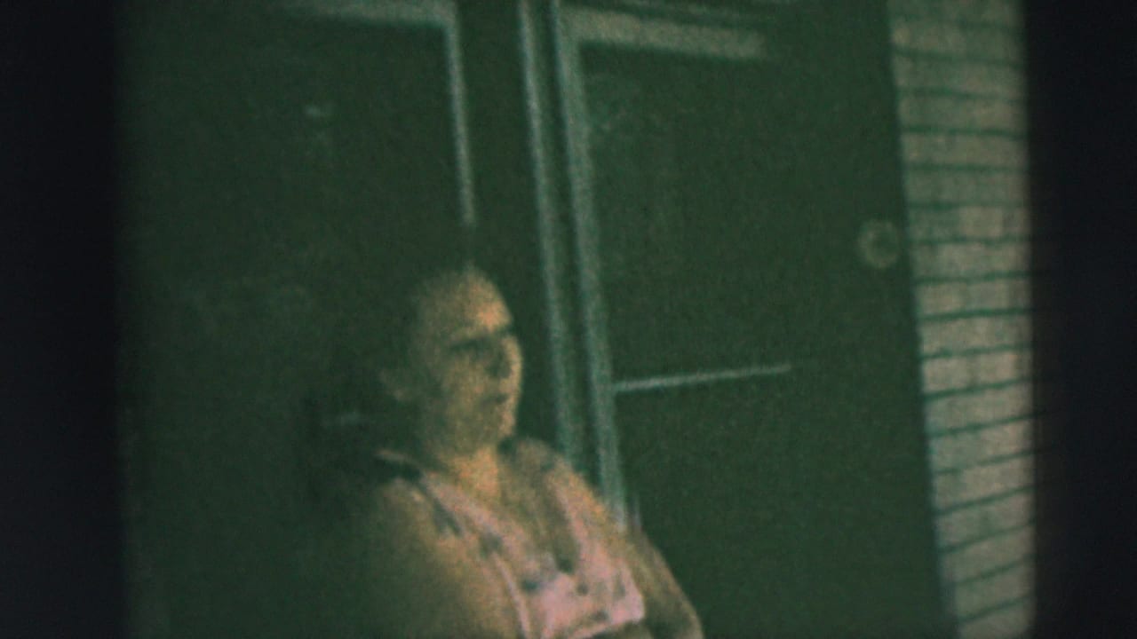 A woman sits on a Camden porch in 1962, softly lit and framed against a brick wall and dark residential doorway.