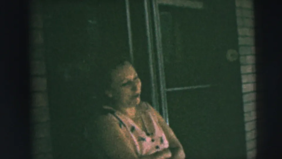 1962 Camden porch footage shows a seated woman in casual summer clothing, filmed handheld against brick and a dark door.