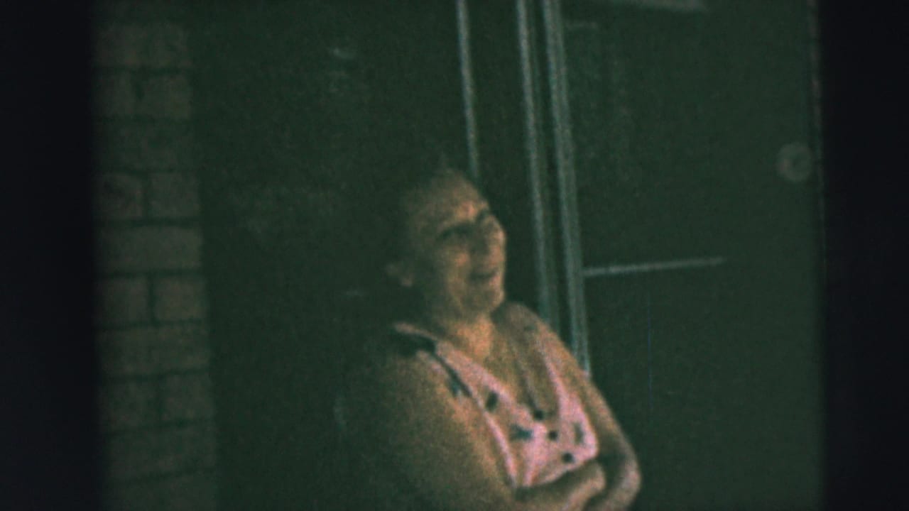 Woman in a pink dress laughs beside a brick porch wall and doorway.
