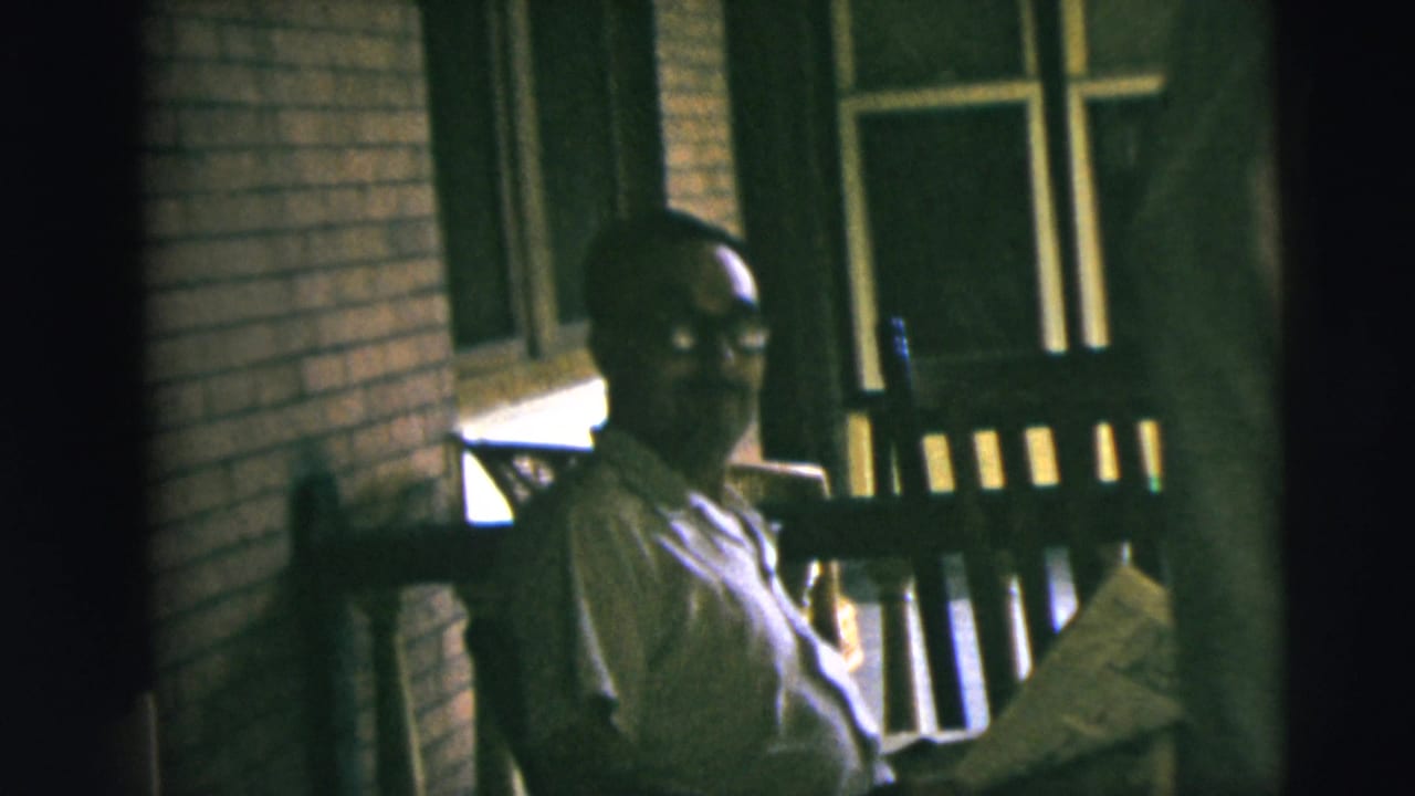 1962 Camden porch scene with a man in a light shirt and glasses turning from his newspaper toward the camera.