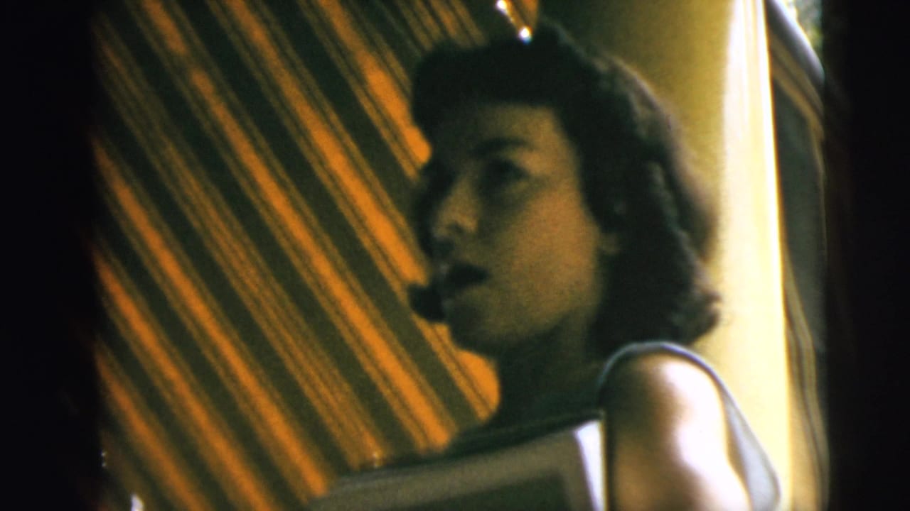 Young woman in profile beside a striped awning, partly lit by warm indoor or porch light.