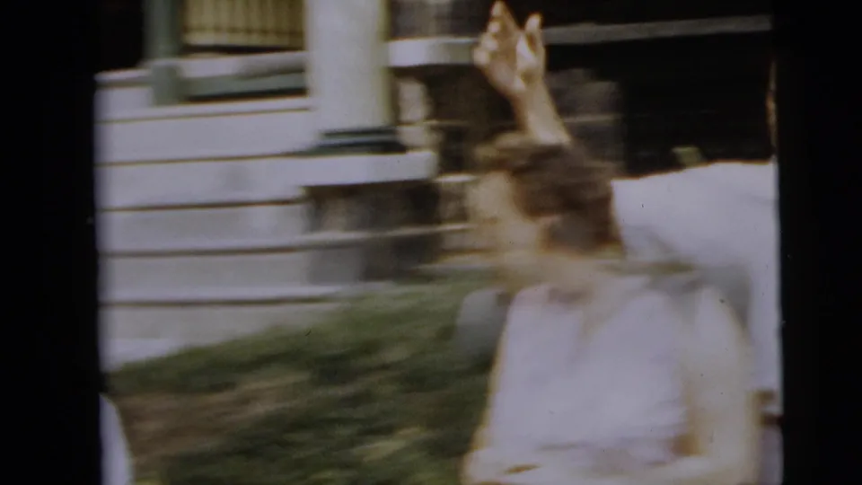 Blurred 8mm frame of the young woman lifting an arm while moving near exterior steps in the Camden home-movie scene.