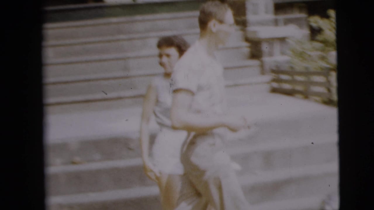 Young man and woman walk past house steps in a soft 8mm frame.
