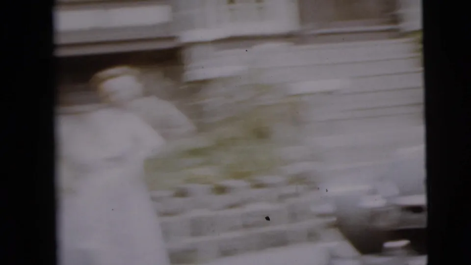 A motion-blurred home-movie frame shows the woman waving beside the parked car and stone-front house.