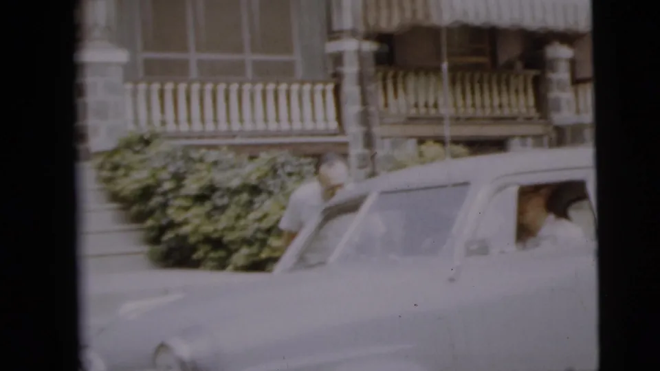 1962 Camden home-movie frame with a man near an older sedan outside a stone and siding residence.