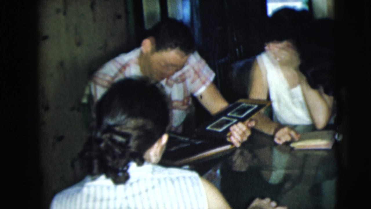 Adults seated around a table looking at a photo album in a dim room.