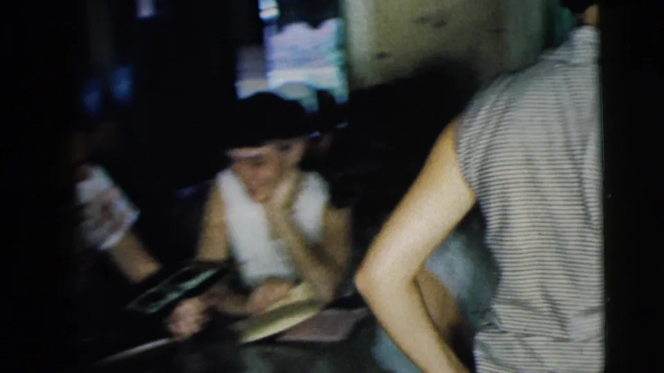 A woman smiles near the table while the album remains open in this soft, handheld 1962 Camden home-movie frame.