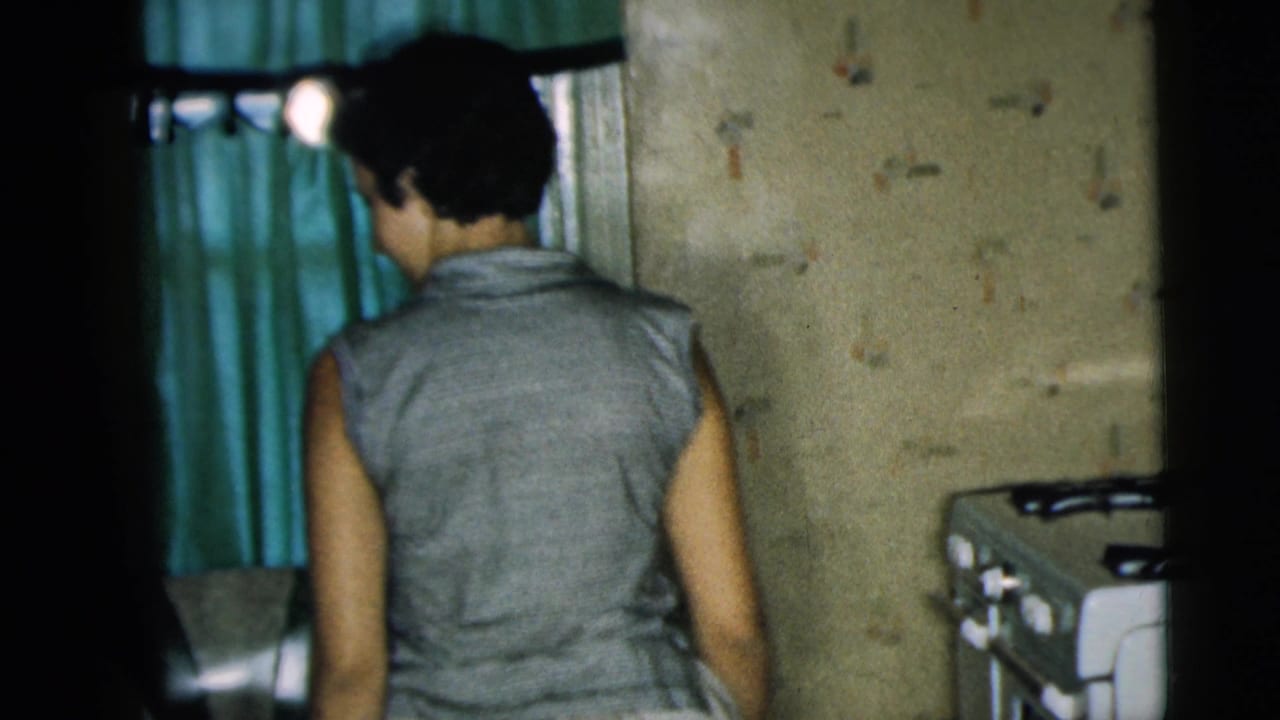 Woman seen from behind entering a room with green curtains and a stove nearby.