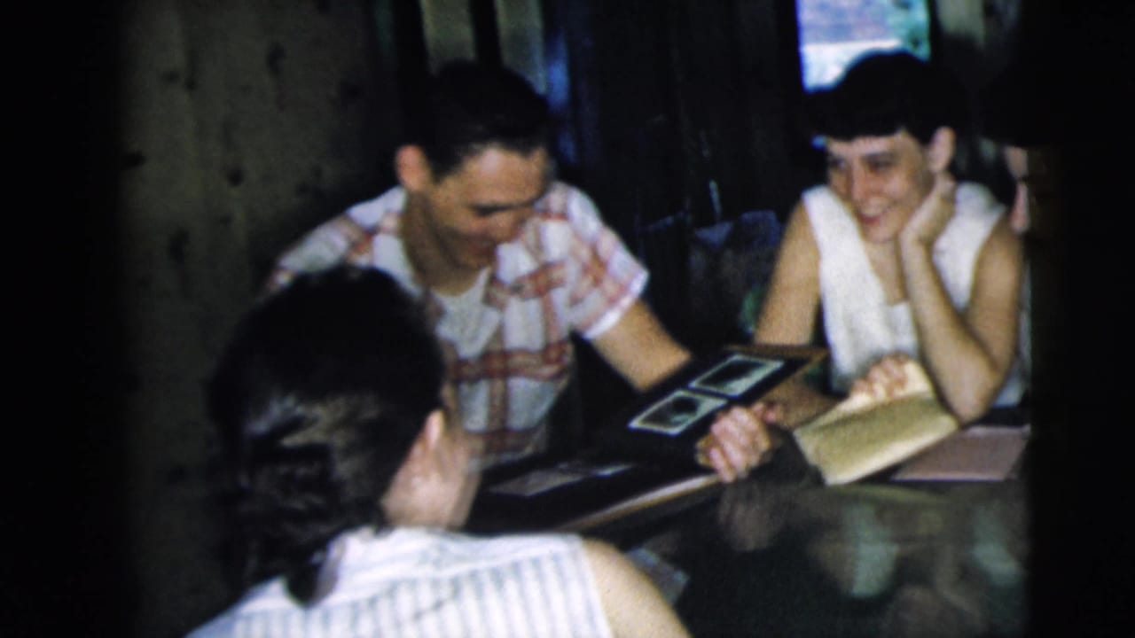Young adults sit around a table looking at photo prints or album pages.