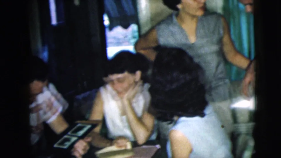 Young adults cluster around a table in a dim Camden interior, with one person standing nearby in a sleeveless top.
