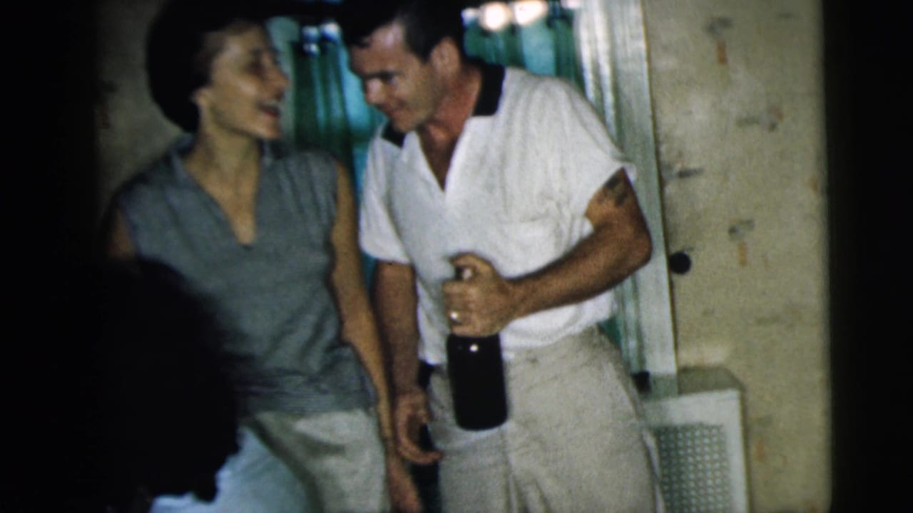 Man holding a dark bottle laughs with a woman in a kitchen doorway.