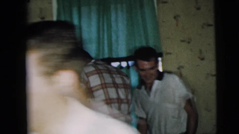 People move through a dim Camden home interior, with motion blur, curtains, and patterned wallpaper visible in the 8mm frame.