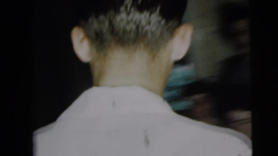A Camden 1962 home-movie frame shows the back of a man's head and white shirt in close handheld view, with another figure partly visible.