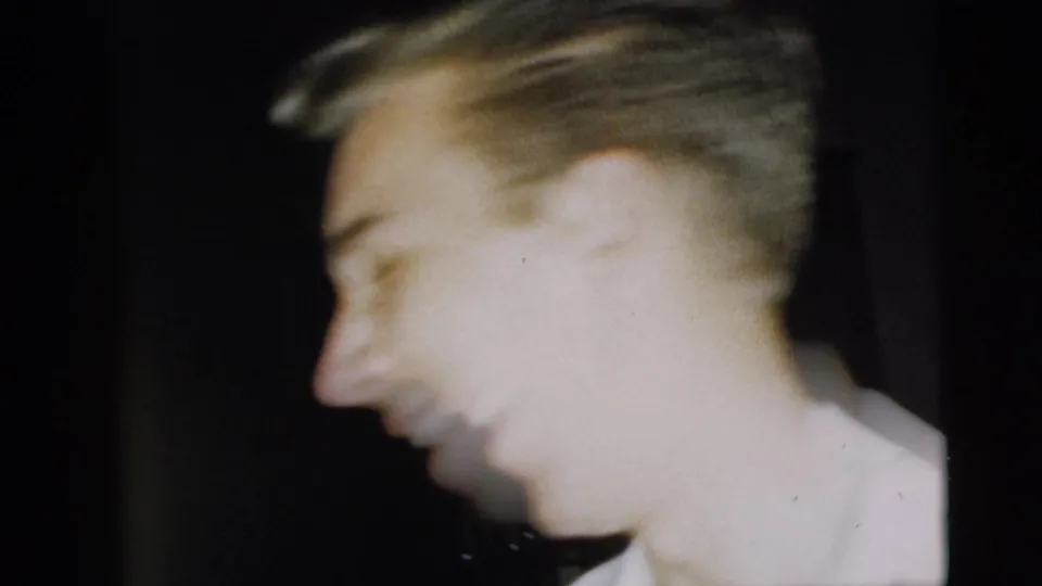 Close handheld 8mm frame of a smiling man in a white shirt, likely during the Camden 1962 reunion described in the clip metadata.