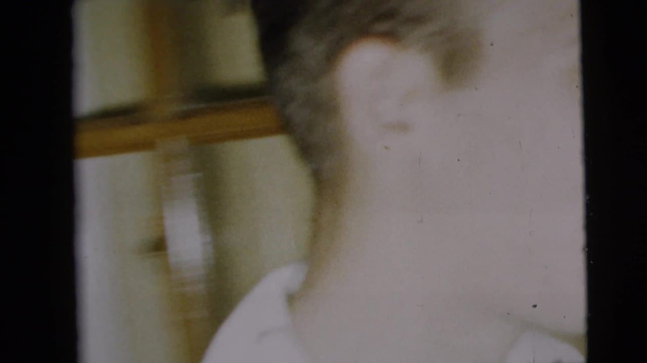 Very soft 8mm close-up of a man in a white shirt inside a private room, with interior trim visible behind him.