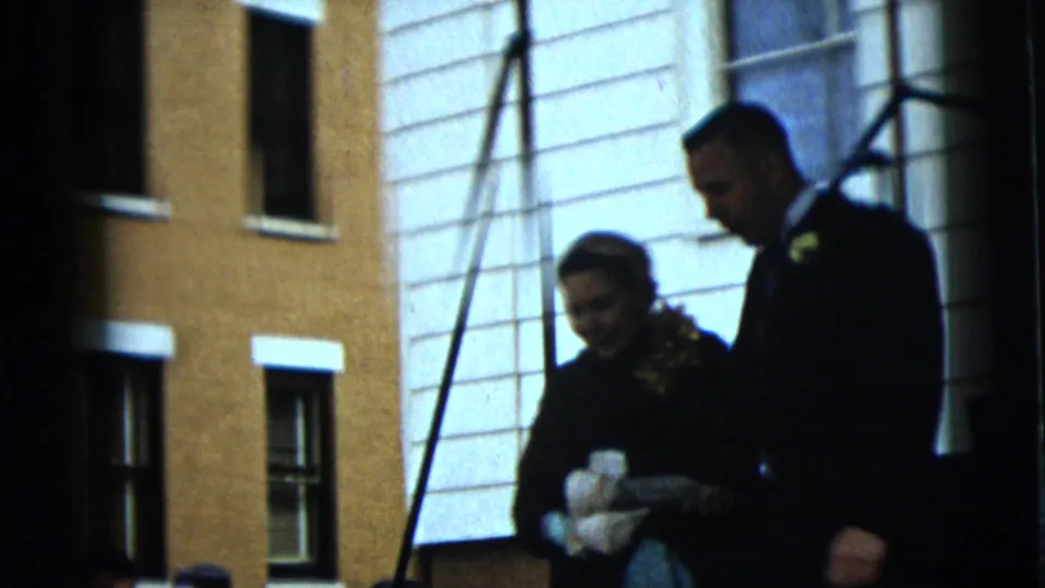 In Camden, New Jersey in 1962, adults in dark coats walk past a yellow brick building with white-trimmed windows.