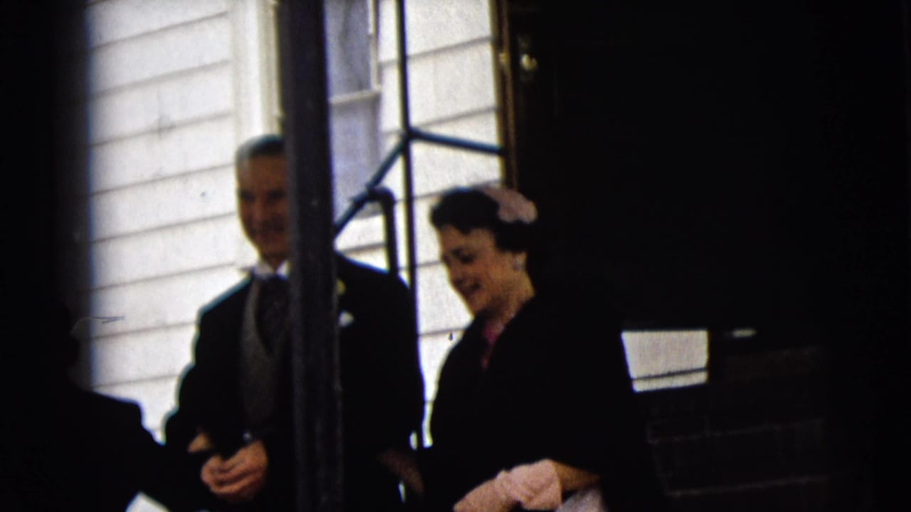 Older formally dressed couple leaving a white-clad building entrance.
