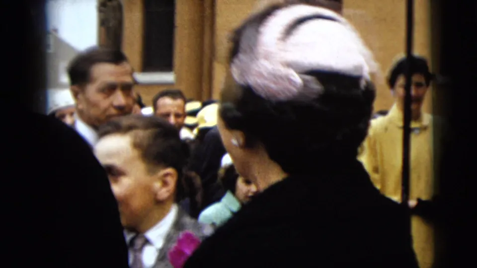 The bride's pink hat is seen from behind as guests and onlookers stand outside the Camden building at the wedding exit.