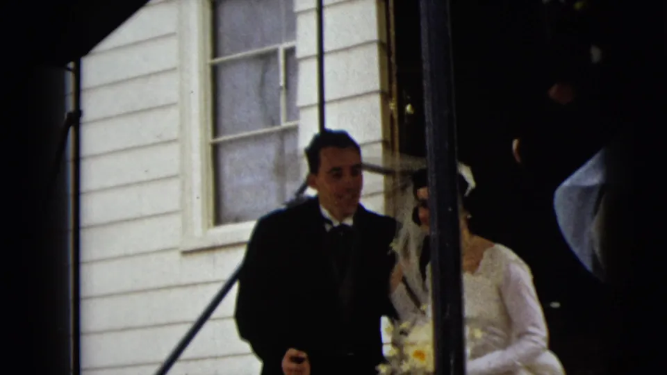 The groom and bride descend the Camden church steps together, with the bride's veil, bouquet, railing, and exterior wall visible.