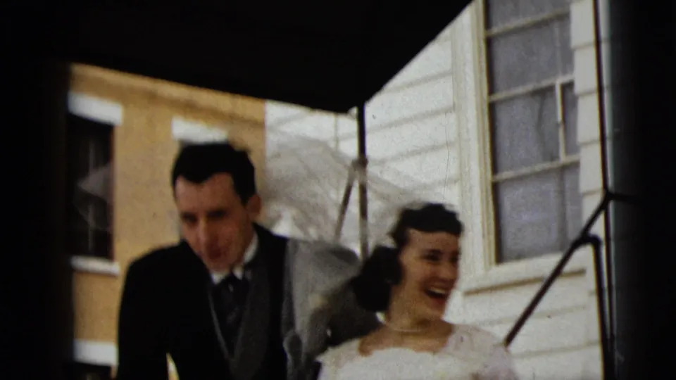 The groom and smiling bride descend exterior steps in the 1962 Camden wedding home-movie footage.