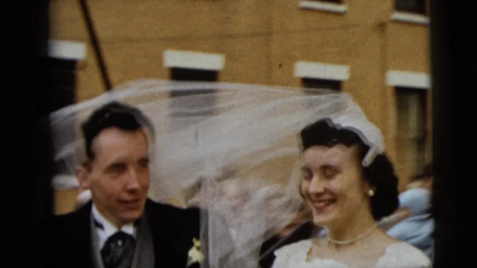 The bride and groom walk outside in Camden, with the bride's veil trailing across the frame and a yellow building behind them.