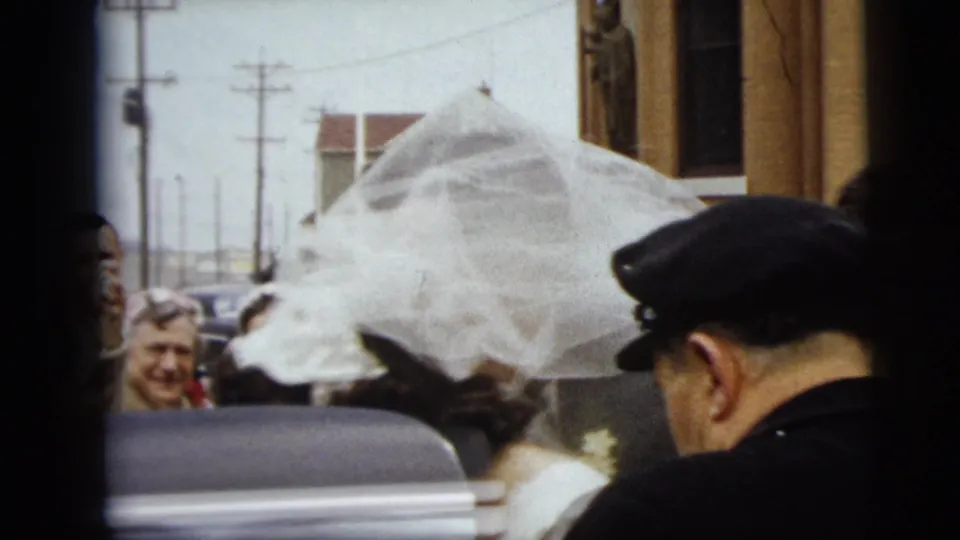 The bride reaches the black car as guests watch nearby in the 1962 Camden wedding departure scene.
