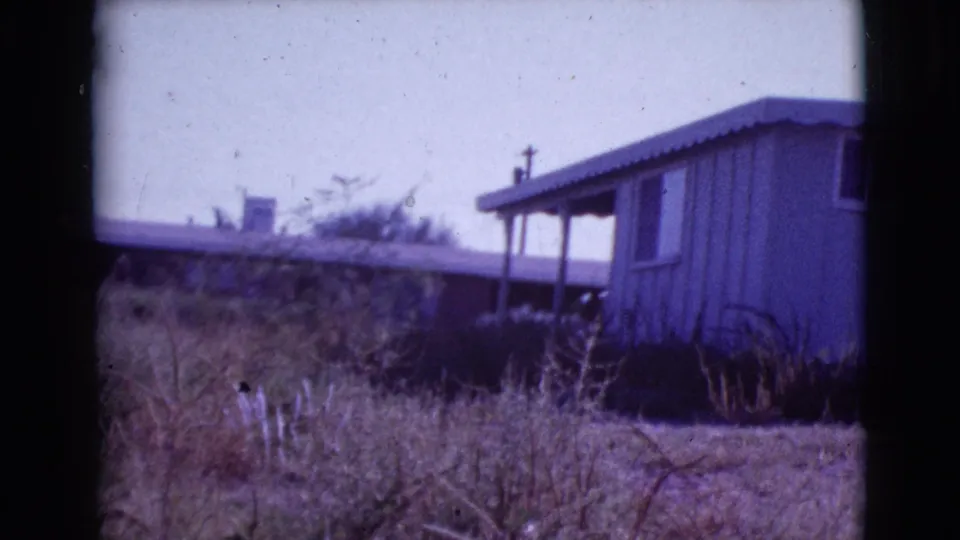 Ranch-style house exterior in Cottonwood, Arizona, with a shaded porch and sparse vegetation in a soft 8mm frame.