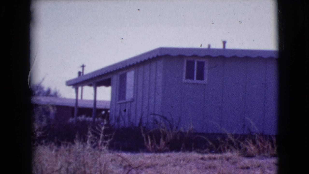 Pale single-story mobile home exterior with porch posts and dry grass in front.