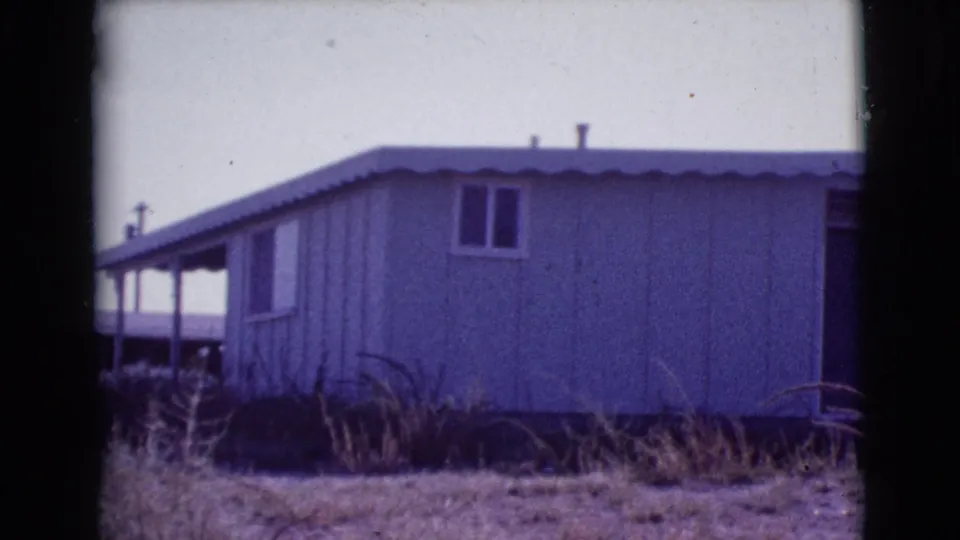 1964 Cottonwood, Arizona frame showing the central exterior of a long pale-sided mobile or prefab home under a bright sky.