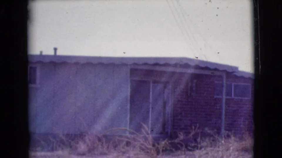 1964 Cottonwood, Arizona view of the same low house, with brick facing, sliding glass door, small window, dry grass, and visible 8mm frame edges.