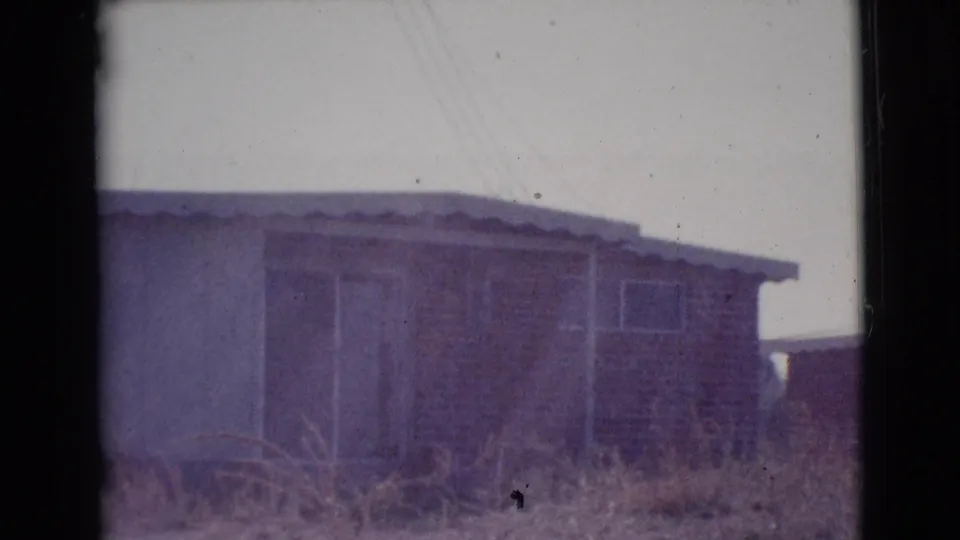 1964 Cottonwood, Arizona frame showing the house exterior in darker exposure, with brick facing, light siding, sliding door, roofline, and dry grass.