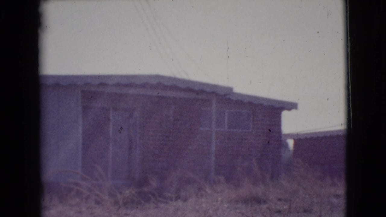 Low single-story house with dry grass in the foreground and a pale sky above.