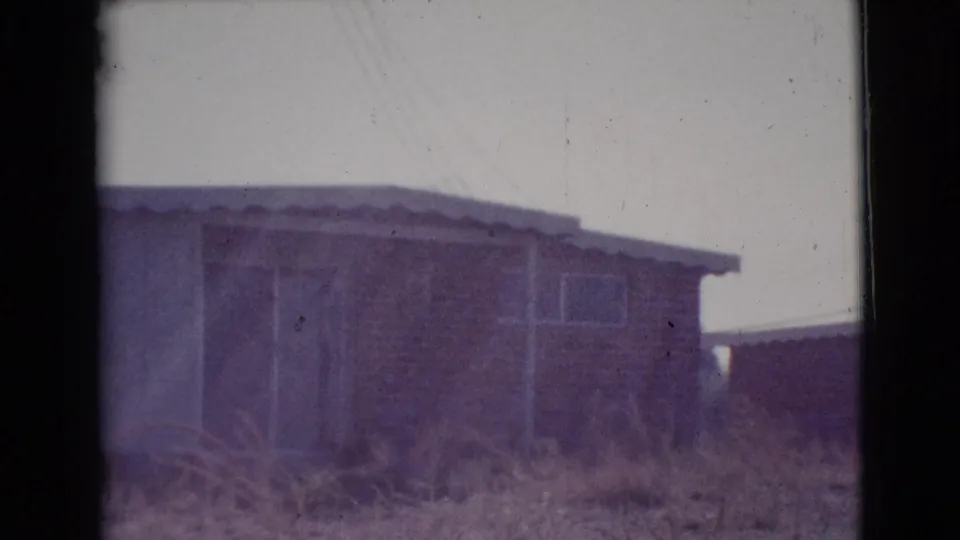 1964 Cottonwood, Arizona home-movie frame showing a modest single-story house, dry grass, simple windows, and soft purple film color.