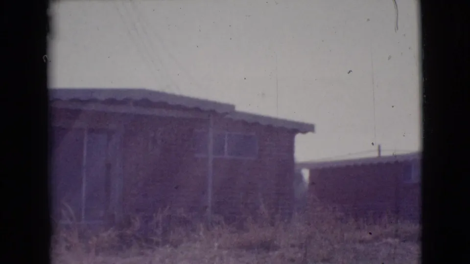 1964 Cottonwood, Arizona exterior view of a low residential structure with simple windows, roof edge, dry weeds, and visible film wear.