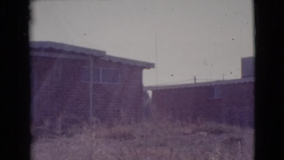 1964 Cottonwood, Arizona home-movie frame showing low residential houses, rough grass, and bright sky.