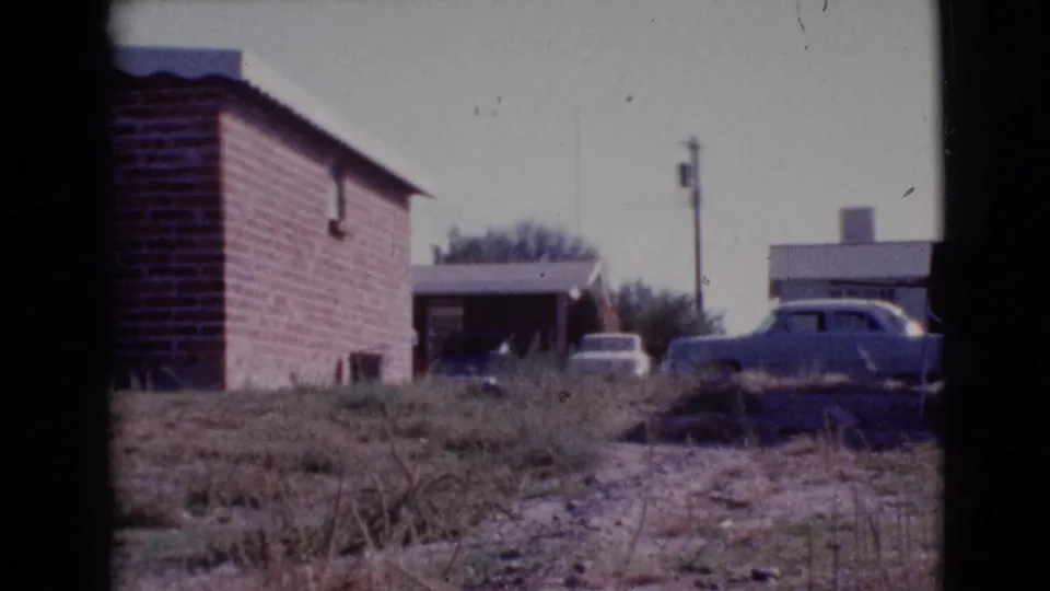 1964 Cottonwood, Arizona frame with a brick house, carport, parked cars, overgrown grass, and a utility pole.