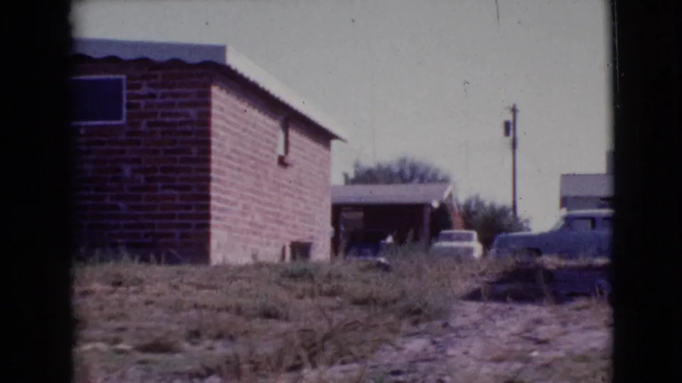 1964 Cottonwood, Arizona home-movie view of a brick house, carport, parked cars, and uneven grassy foreground.