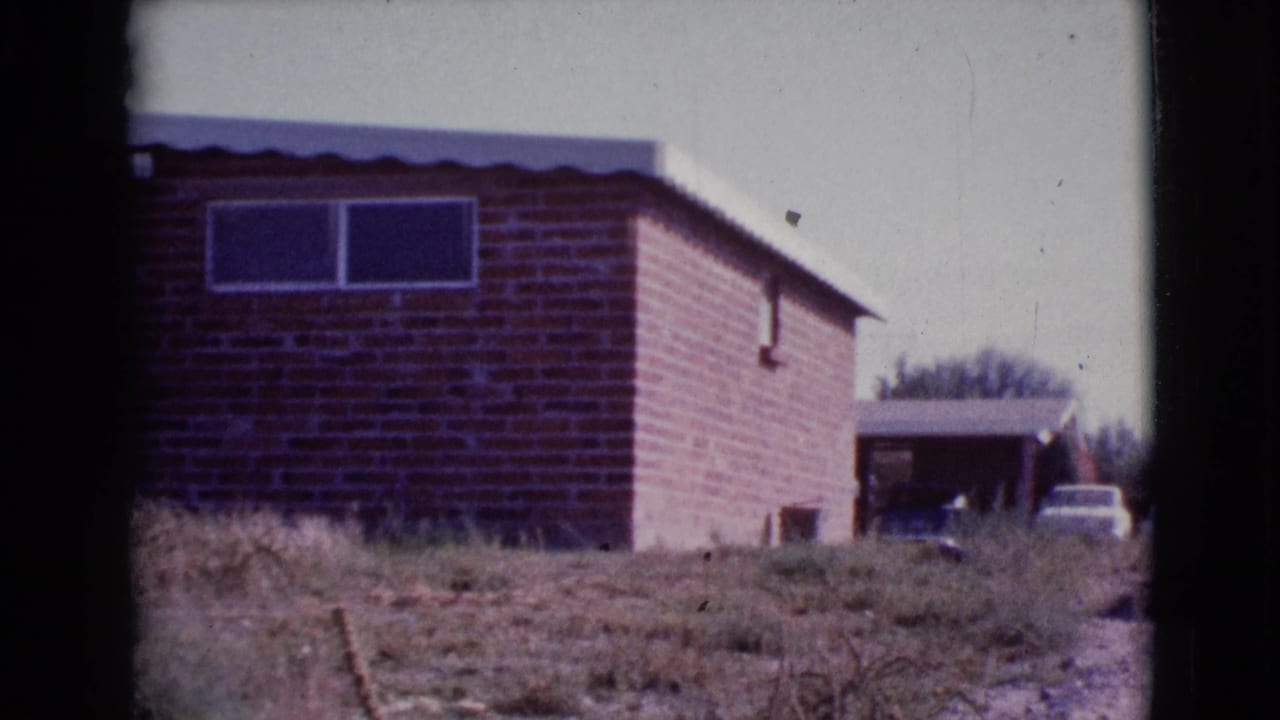 Small brick house seen across dry grass with two high windows and a pale sky.