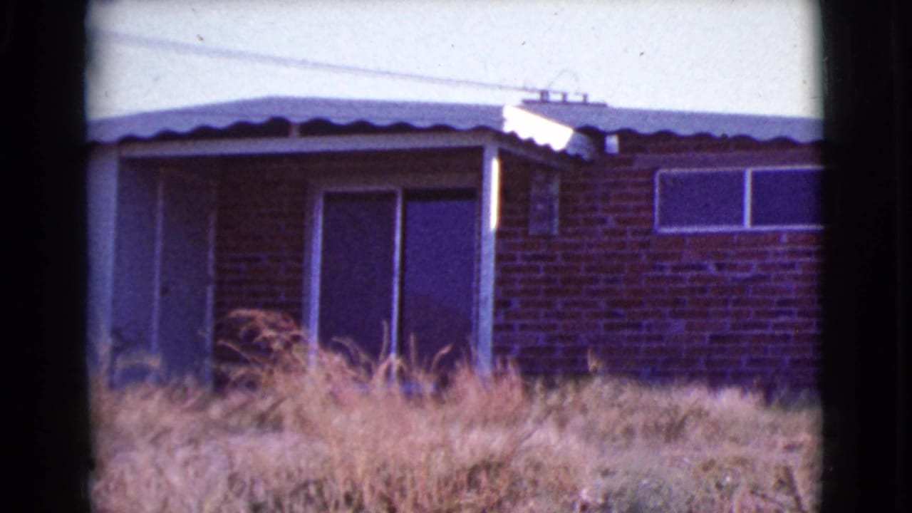 Small brick-and-siding house with sliding glass doors behind dry grass.