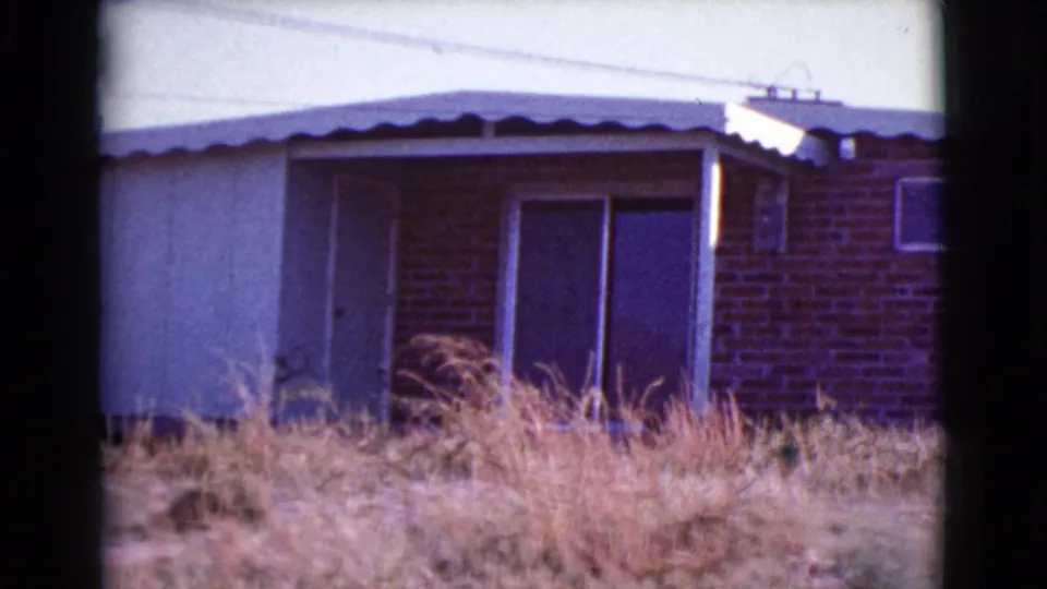 A 1964 Cottonwood, Arizona exterior view shows the house frontage, porch post, brick wall, sliding doors, and dry grass across the foreground.