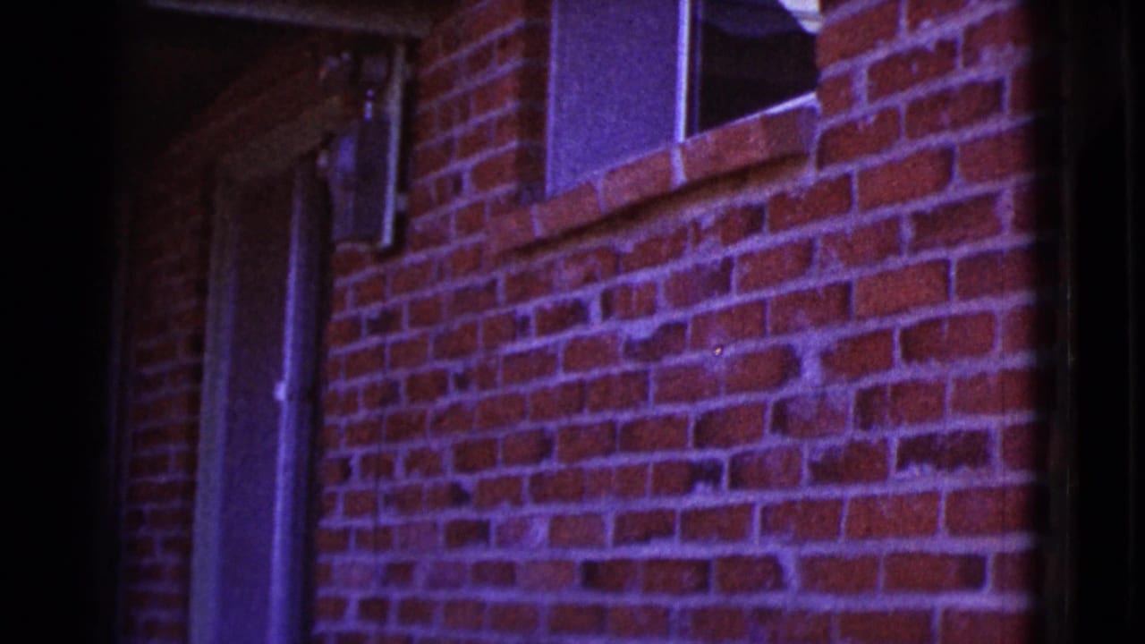 Red brick wall with a small window, vertical pipe, and dark film edges.