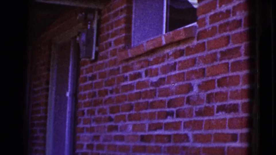 1964 Cottonwood, Arizona 8mm frame showing a red brick exterior wall with a small window, pipe, and strong purple color shift.