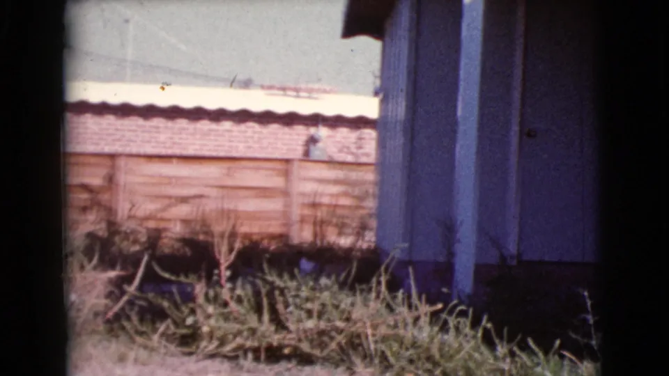 1964 Cottonwood, Arizona frame with a wooden fence, dry vegetation, and the side edge of a house exterior.