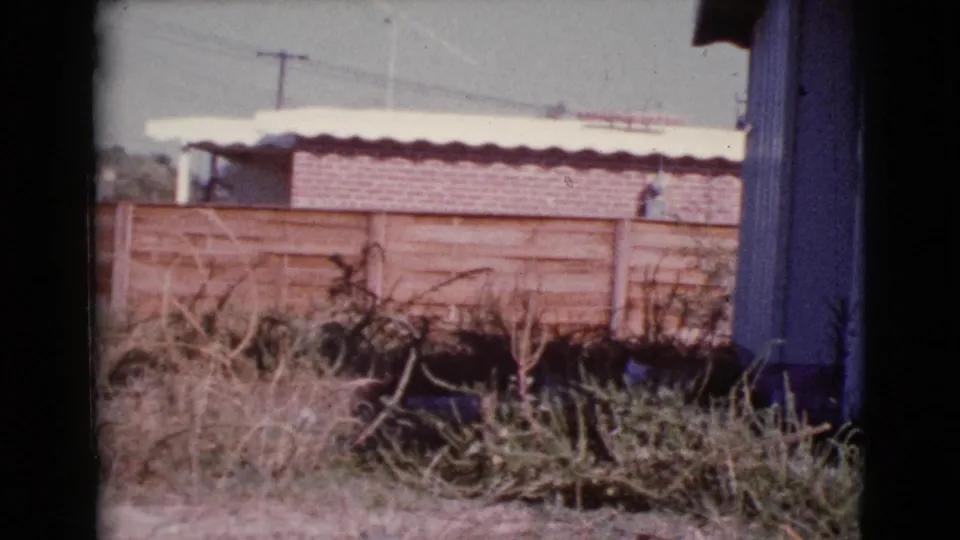 Cottonwood, Arizona 1964 home-movie frame showing a wooden fence, dry yard, brick section, and utility pole.